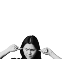 Young woman with black hair and a black shirt has a finger in each of her ears to try and block out sound. Her eyes are closed and she looks overwhelmed.