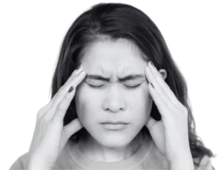 Young Asian woman with black hair with her hands against her head. Her eyes are closed and she looks overwhelmed.