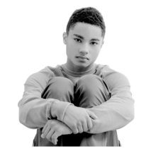 Black and white image of young man sitting with his knees up to his chest and his arms wrapped around his legs.