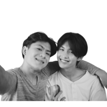 Two people smiling and posing for a selfie. On the right a person smiling with short black hair and on the left a person with short black hair with their arm around person on the right.