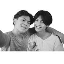 Two people smiling and posing for a selfie. On the right a person smiling with short black hair and on the left a person with short black hair with their arm around person on the right.