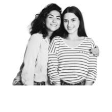 Two women pose for a picture together, smiling at the camera. The one on the left has curly dark hair and has her arm around the woman on the right who has straight dark hair and is wearing a striped shirt.