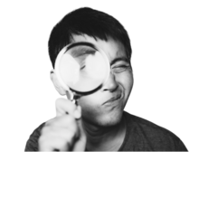 A young man with dark hair looks through a magnifying glass at the camera